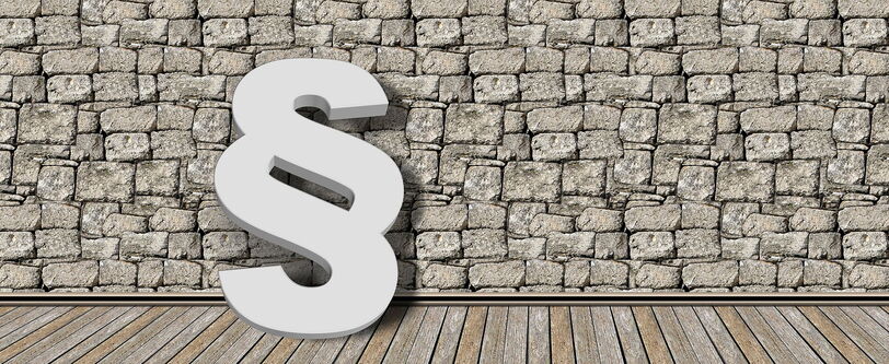 Ein Paragraphenzeichen auf einem Holzweg, an einer Mauer gelehnt