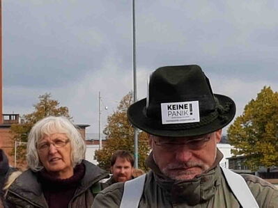 Mann mit schwarzem Hut an dem ein Schildchen klebt.