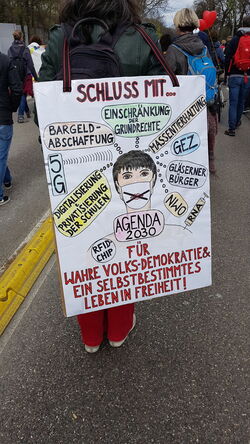 Frau mit großem Plakat. Mittig eine Person mit Maske > X für keine.