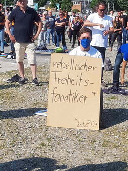 Junger Mann mit blauer Maske um Mund und Nase und großem Karton-Plakat